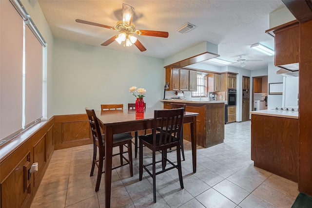 dining space featuring visible vents, a wainscoted wall, a ceiling fan, a textured ceiling, and light tile patterned floors