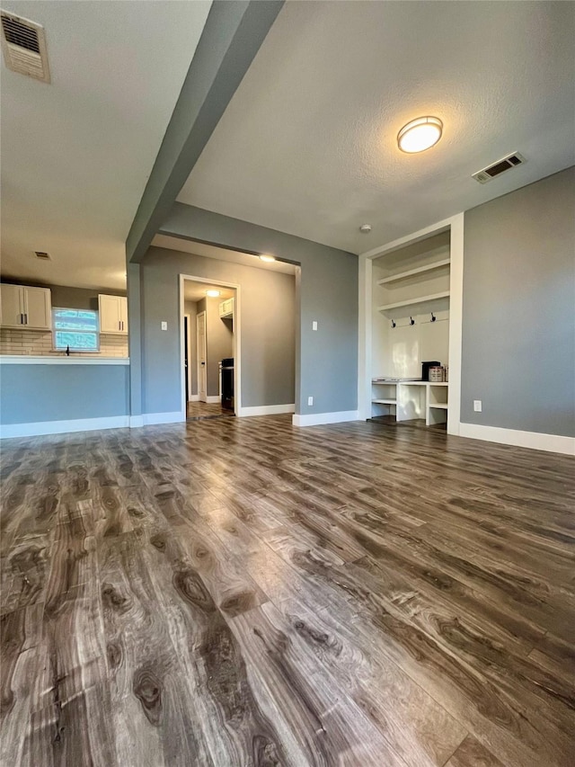 unfurnished living room featuring visible vents, a textured ceiling, and dark wood finished floors
