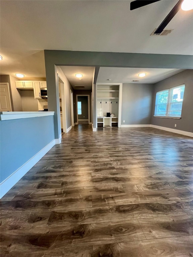 unfurnished living room with dark wood finished floors, visible vents, a ceiling fan, and baseboards