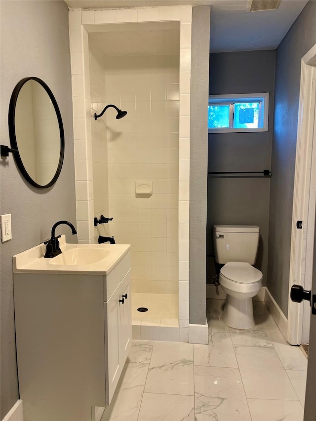 bathroom with toilet, marble finish floor, a tile shower, baseboards, and vanity