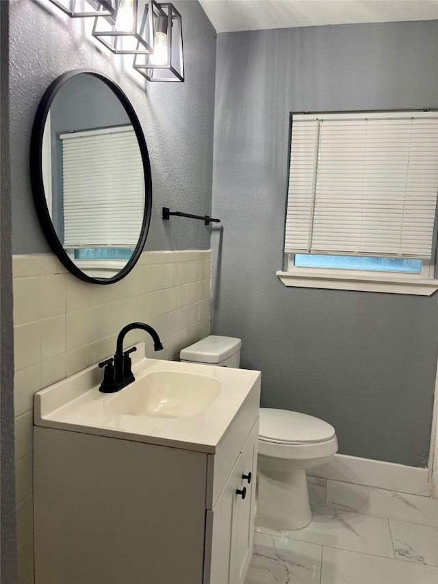bathroom with baseboards, toilet, vanity, marble finish floor, and tile walls