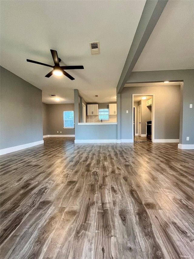 unfurnished living room with baseboards, visible vents, dark wood-style flooring, and ceiling fan