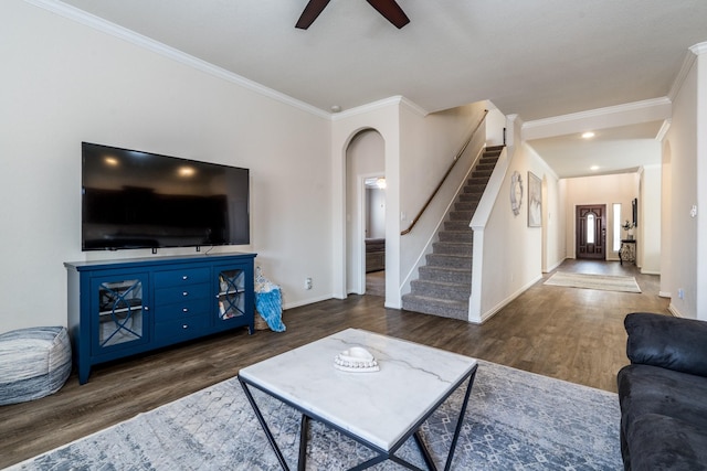 living room featuring dark wood-type flooring, arched walkways, crown molding, and stairs
