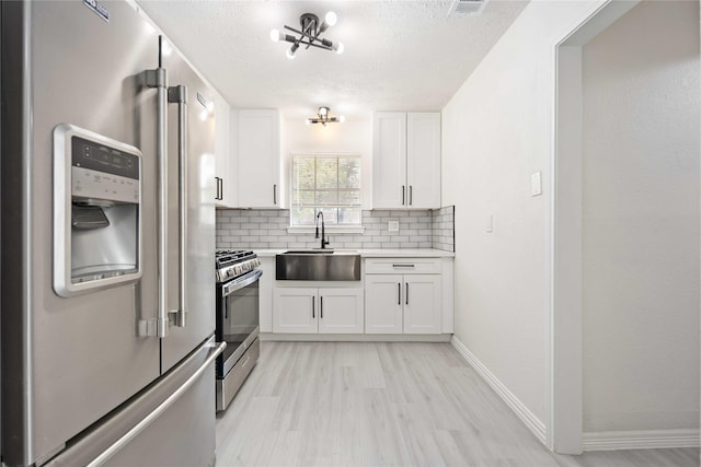 kitchen with a sink, tasteful backsplash, stainless steel appliances, white cabinets, and light countertops