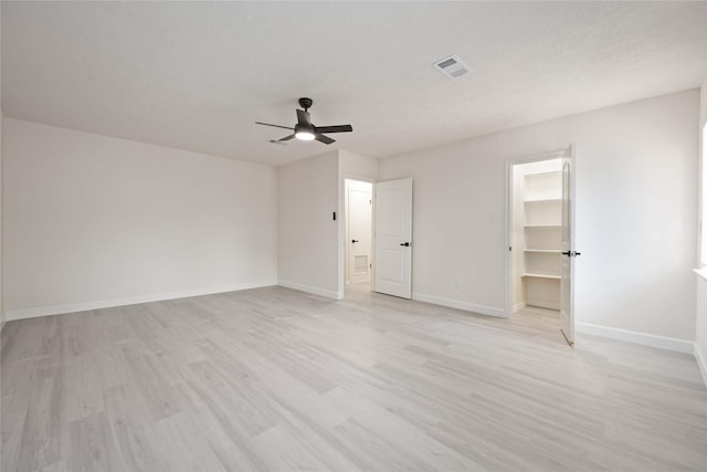 unfurnished bedroom with visible vents, a walk in closet, baseboards, ceiling fan, and light wood-style flooring