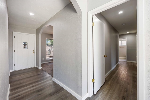 hall featuring dark wood finished floors, recessed lighting, arched walkways, and baseboards