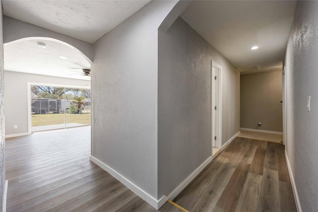 hall with baseboards, arched walkways, and wood finished floors