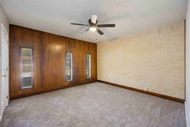empty room featuring wooden walls, baseboards, brick wall, ceiling fan, and carpet flooring
