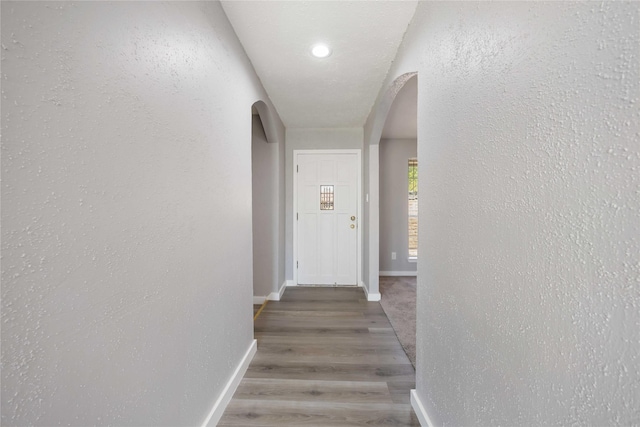 corridor with wood finished floors, baseboards, arched walkways, and a textured wall