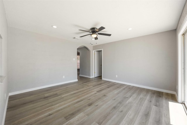 spare room featuring visible vents, baseboards, ceiling fan, light wood-style flooring, and arched walkways
