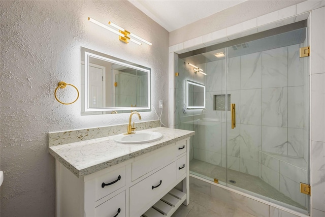 bathroom featuring vanity, a textured wall, and a stall shower