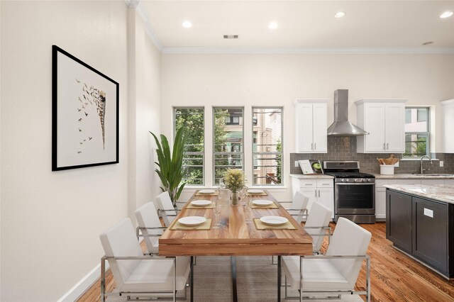 4314 Gibson St Unit A, Houston, TX 77007 - kitchen with stainless steel gas range oven, wall chimney range hood, ornamental molding, light wood-style floors, and white cabinetry
