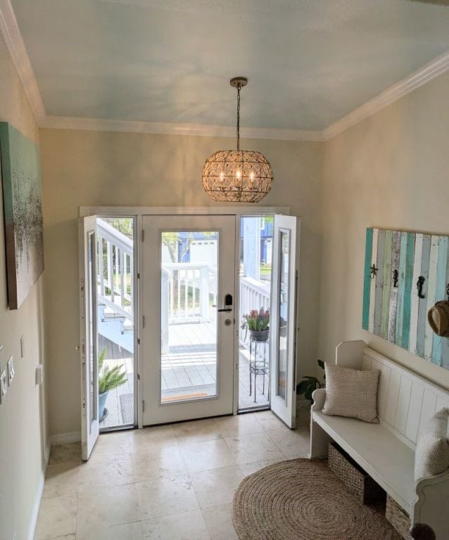 foyer entrance with crown molding, a notable chandelier, and baseboards