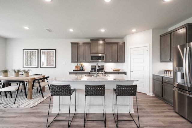 kitchen featuring light stone counters, appliances with stainless steel finishes, wood finished floors, and a sink