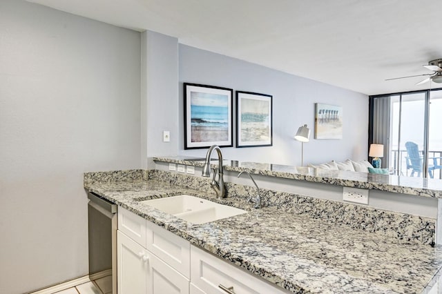 kitchen featuring a ceiling fan, light stone countertops, white cabinetry, a sink, and stainless steel dishwasher