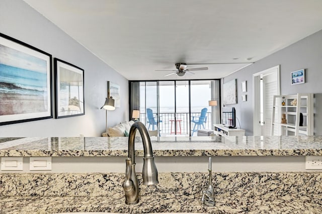 kitchen with a sink, light stone counters, open floor plan, and ceiling fan