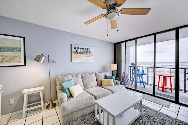 tiled living room featuring baseboards, a wall of windows, and a ceiling fan