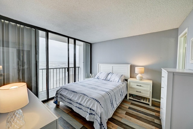 bedroom with access to exterior, a textured ceiling, wood finished floors, and expansive windows