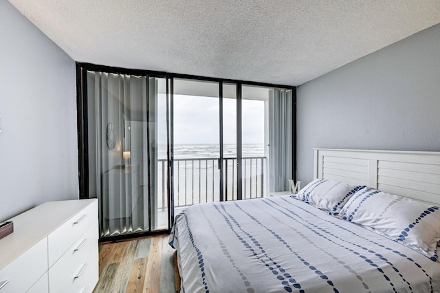 bedroom with floor to ceiling windows, a textured ceiling, light wood-style floors, and access to outside