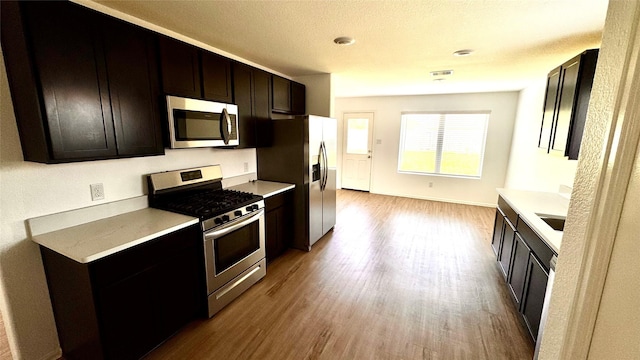 14407 Woodcott Warren Way, Rosharon, TX 77583 - kitchen featuring appliances with stainless steel finishes, wood finished floors, light countertops, baseboards, and a sink