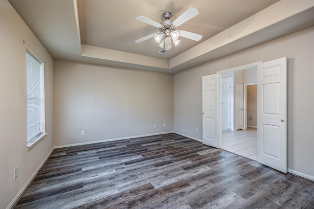unfurnished bedroom featuring visible vents, baseboards, a raised ceiling, and wood finished floors