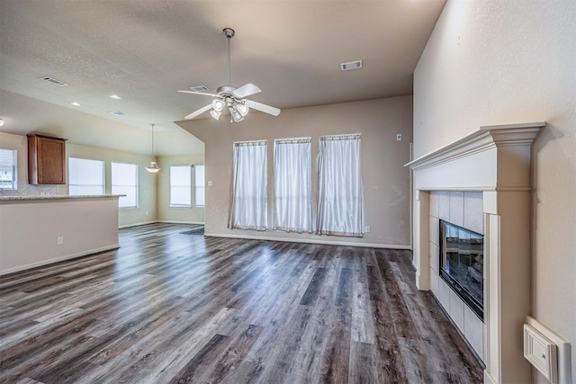 unfurnished living room with a tiled fireplace, ceiling fan, dark wood-type flooring, and visible vents