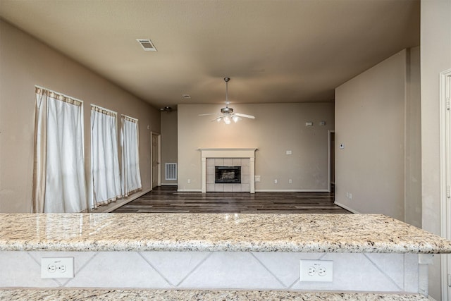 unfurnished living room with visible vents, dark wood finished floors, ceiling fan, and a tile fireplace