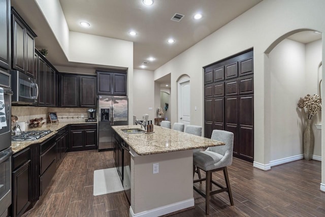 24146 Valencia Ridge Ln, Katy, TX 77494 - kitchen with light stone counters, a breakfast bar, dark wood finished floors, arched walkways, and stainless steel appliances