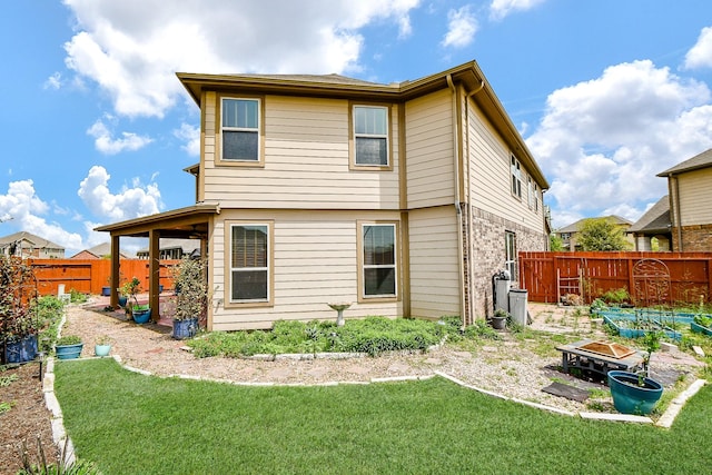 back of house with a lawn, a fenced backyard, a fire pit, and a patio