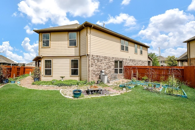 rear view of house featuring a lawn, a fenced backyard, a fire pit, and a vegetable garden