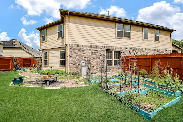 back of house with a fenced backyard, brick siding, a lawn, and a vegetable garden