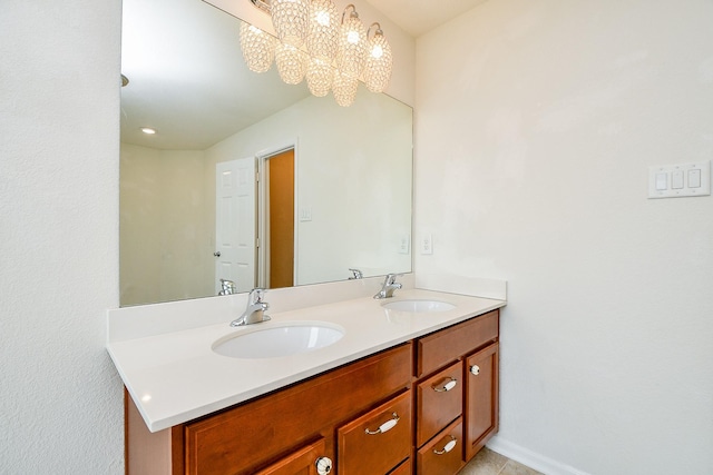 bathroom featuring an inviting chandelier, a sink, double vanity, and baseboards