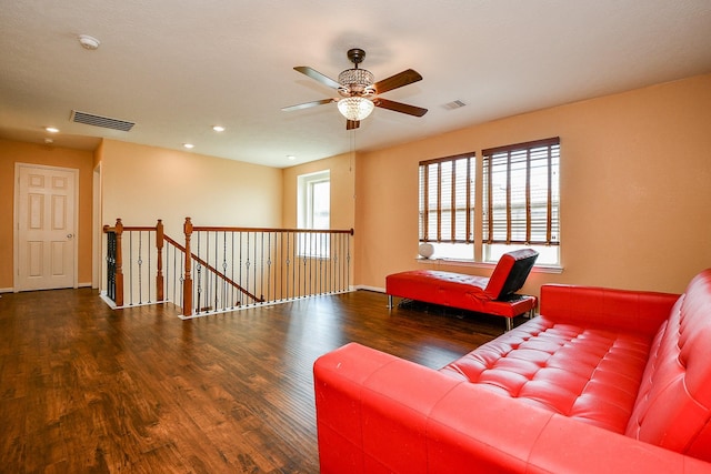 living area with wood finished floors, visible vents, a ceiling fan, and an upstairs landing