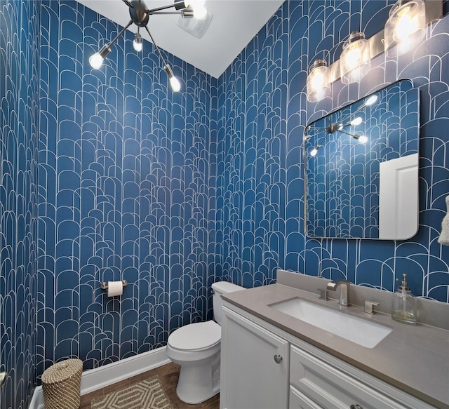 bathroom featuring toilet, vanity, baseboards, and wallpapered walls