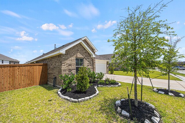 view of side of property with brick siding, an attached garage, fence, and a lawn
