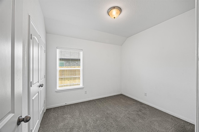 unfurnished bedroom featuring dark carpet, baseboards, and lofted ceiling