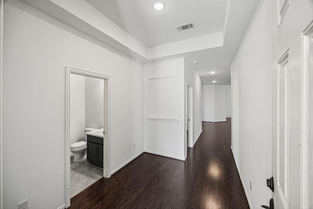 hall with dark wood-type flooring, a raised ceiling, visible vents, and recessed lighting
