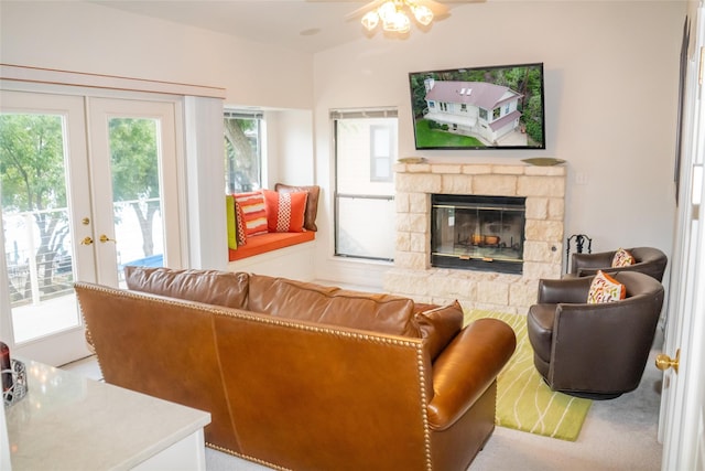 carpeted living area with a healthy amount of sunlight, french doors, and a stone fireplace