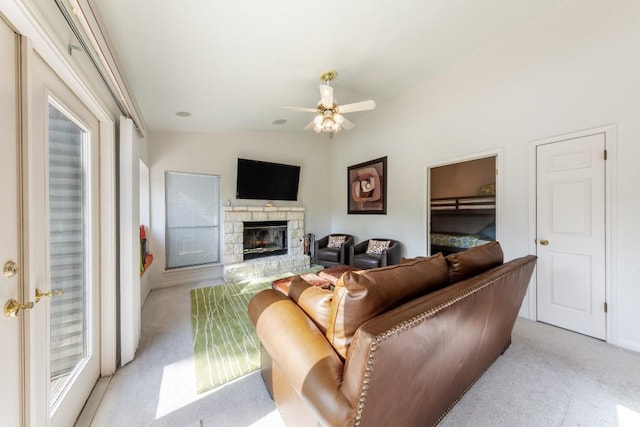living area with ceiling fan, lofted ceiling, light carpet, and a stone fireplace