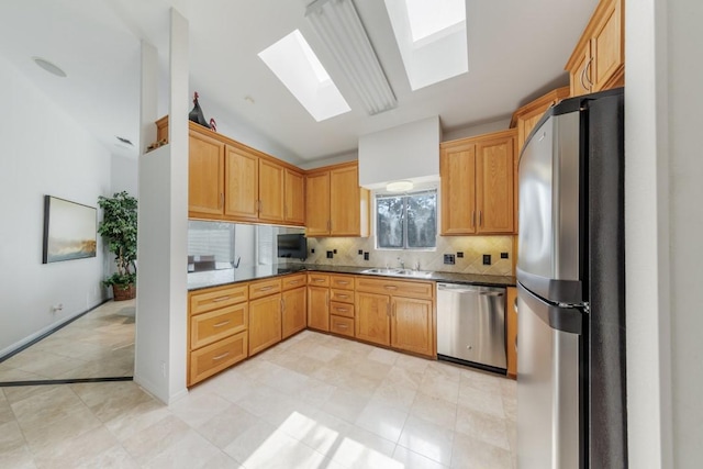 kitchen featuring appliances with stainless steel finishes, decorative backsplash, a sink, and vaulted ceiling with skylight