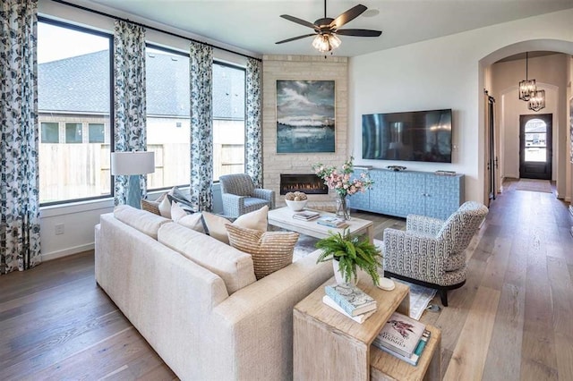 living area featuring arched walkways, a ceiling fan, wood finished floors, and a healthy amount of sunlight