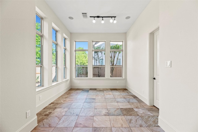 unfurnished sunroom with visible vents, baseboards, track lighting, and stone finish flooring