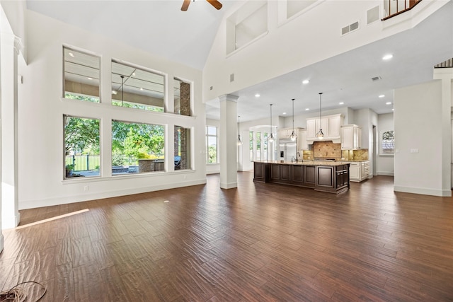 living room featuring ceiling fan, decorative columns, visible vents, a high ceiling, and baseboards