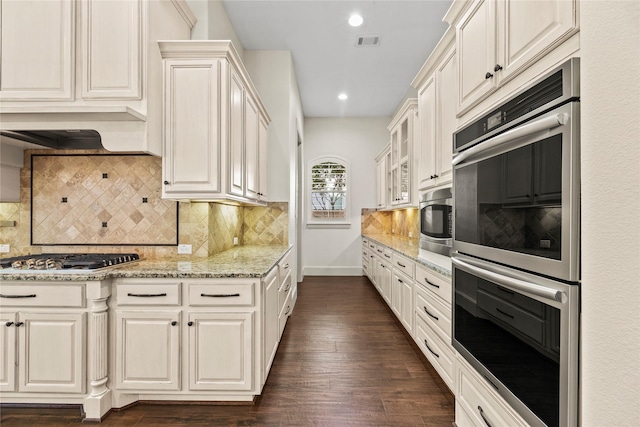 kitchen with visible vents, glass insert cabinets, stainless steel appliances, decorative backsplash, and light stone counters