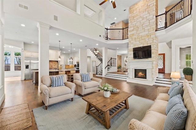 living area with light wood-type flooring, a towering ceiling, a ceiling fan, visible vents, and stairway