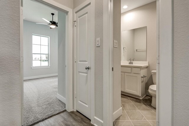 half bathroom with vanity, a ceiling fan, baseboards, toilet, and a textured wall