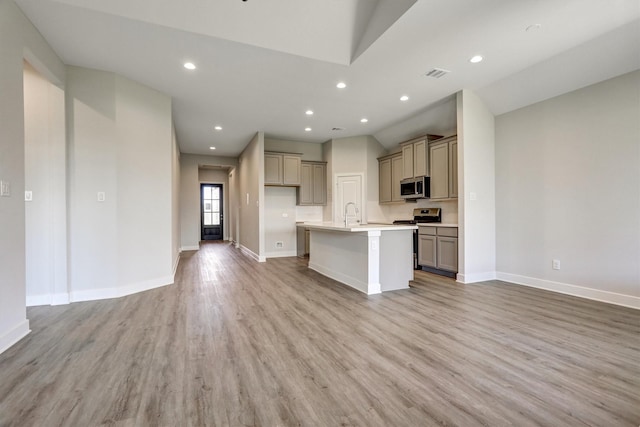 kitchen featuring a kitchen island with sink, recessed lighting, appliances with stainless steel finishes, light wood finished floors, and baseboards