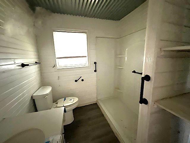 bathroom with toilet, wood finished floors, and walk in shower
