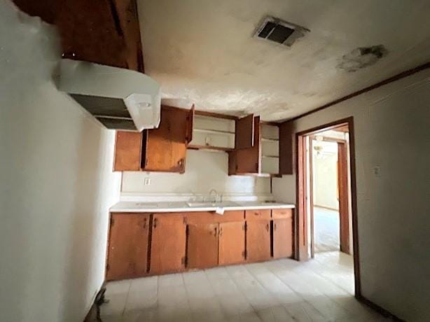 kitchen featuring a sink, visible vents, brown cabinetry, and light countertops