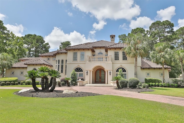 mediterranean / spanish-style home featuring a front yard, a balcony, stucco siding, and a tile roof